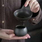 Handmade black clay tea strainer with spherical base on white background