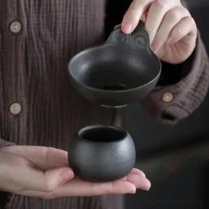 Handmade black clay tea strainer with spherical base on white background
