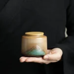 front view of handcrafted ceramic tea canister with bamboo lid and mountain landscape pattern